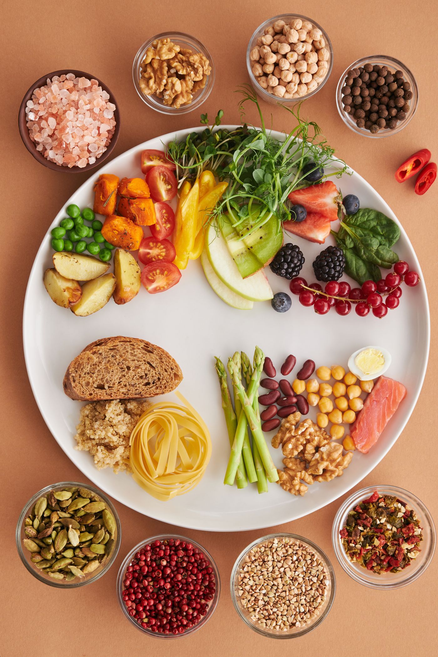 A balanced plate of vegetables, fruit, whole grains, legumes, nuts and fish surrounded by spices and seeds