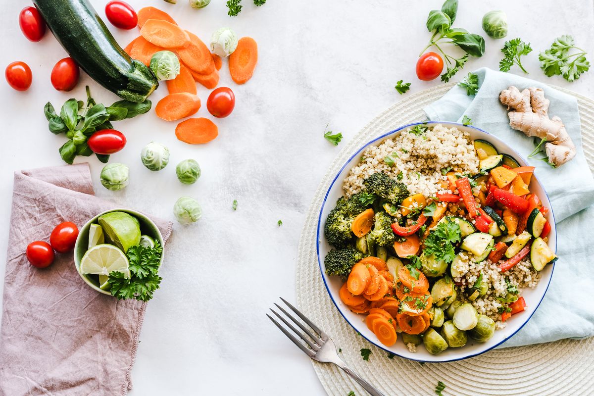 A colourful bowl of quinoa with roasted vegetables beside fresh produce